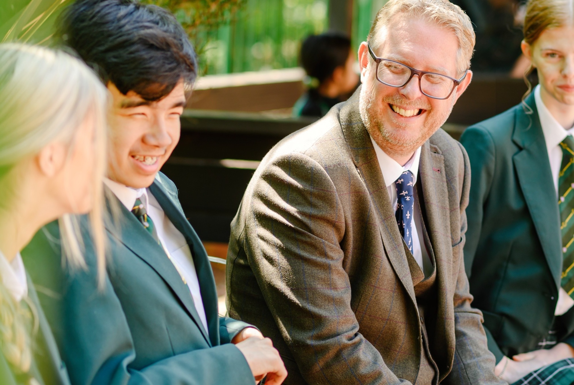 Head teacher John Sample sits on a bench interacting with pupils.