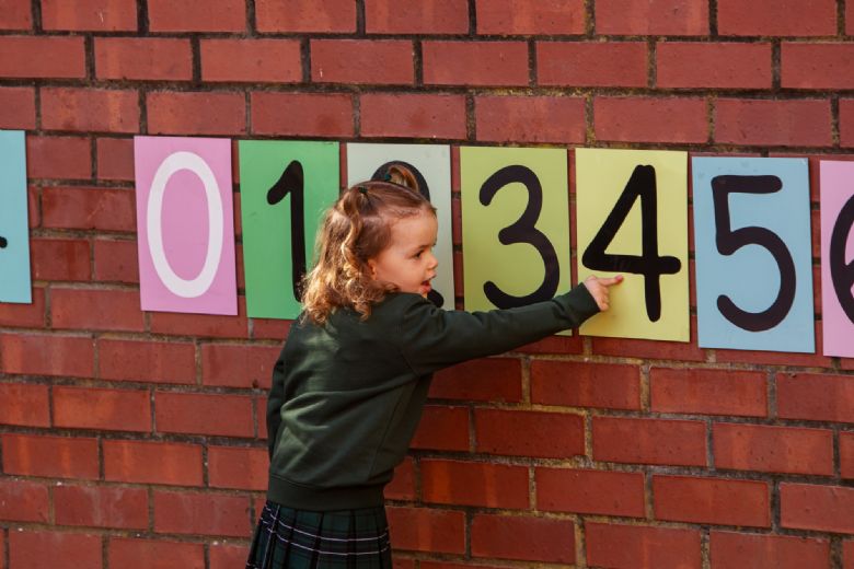 A young girl in Argyle House School uniform counts numbers 1-10 from coloured cards on a wall.